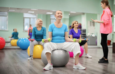 Group of mature women with young coach training in modern gym