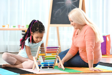 Female mature nanny teaching little African-American girl to count using abacus