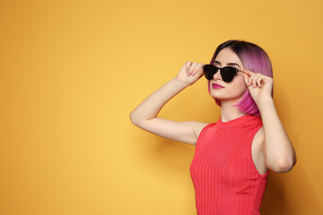 Young woman with trendy hairstyle wearing sunglasses against color background