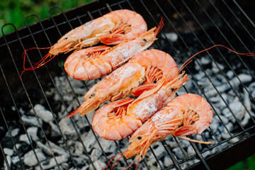 Langoustine and shrimp are grilled. The woman turns the shrimps forceps with chef tongs, sprinkles them with half-lemon juice