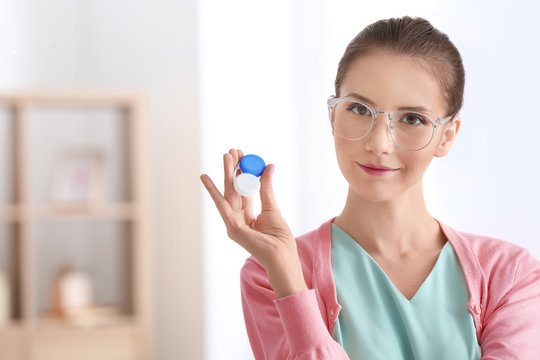 Woman wearing glasses and holding plastic container with contact lenses, indoors