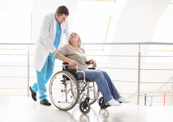 Fototapeta premium Male doctor taking care of mature woman in wheelchair indoors