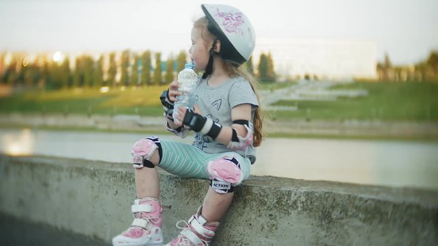 A little girl in a helmet and defense skates on roller skates. The child rolls on the rollers in the park. Girl learns to ride a roller skate.