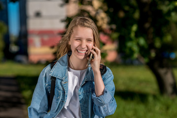 Girl schoolgirl talking on the phone, in summer in nature, smiling happily, emotionally happy. In her hands holds a smartphone, in denim jacket.