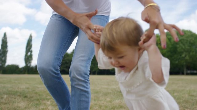 Young mother holds her daughters hands as she walks in a park, in slow motion