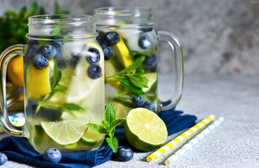 Lemonade with lime, lemon and blueberries on a stone background. Summer cold drink.