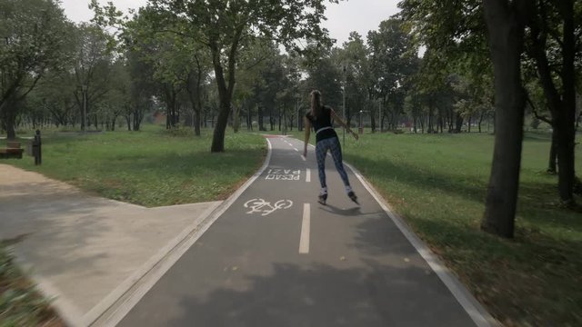 White handsom brown hair girl in tight blue pants woman riding roller skates on bike road in park, during summer day