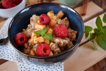 Porridge with apples, raspberries and honey topped with mint. Healthy breakfast meal