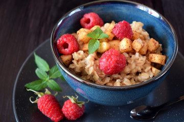 Porridge with apples, raspberries and honey topped with mint. Healthy breakfast meal