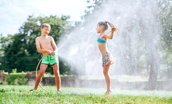 Brother and sister play together with watering hose in garden