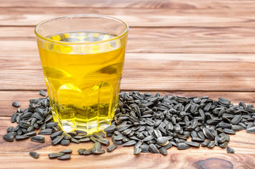 Glass of cooking oil with heap of sunflower seeds on wooden background.