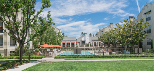 Common apartment building complex in Palo Alto, California, USA with fenced guard swimming pool. Summer cloud blue sky
