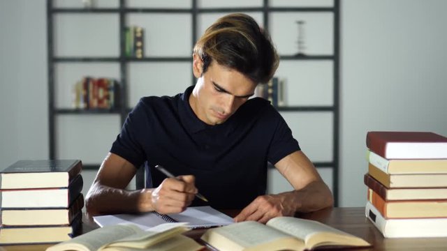 Young student preparing for lessons in the library. Writting notes, reading books.