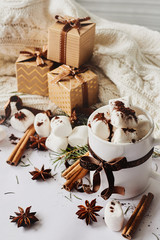Winter Christmas New Year hot drink. Cup of hot chocolate or cocoa with marshmallow, gift boxes with ribbon, fir branch, star anise, cinnamon on white knitted background