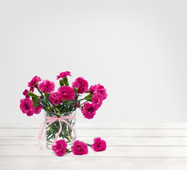 Bouquet of flowers pink carnations ( Dianthus caryophyllus ) in small vase on white wooden table on light background with space for text
