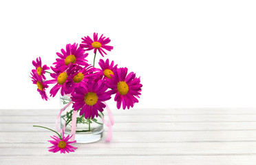 Bouquet of flowers pink daisies ( Pyrethrum, Tanacetum coccineum ) in small vase on white wooden table on white background with space for text