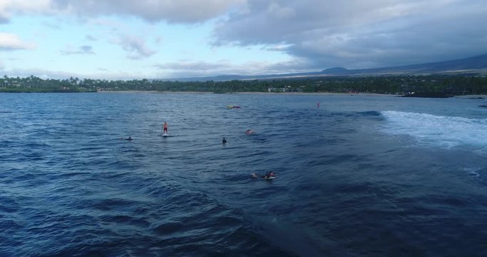 Slow motion aeril footage of a man surfing a wave with a long beach and a conoe in the background in Kailua Kona, Hawaii.