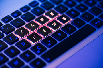 Fake news written on a backlit keyboard in a blue ambiant light - 216294501