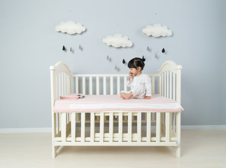 Beautiful little girl sits on white blanket in her bedroom