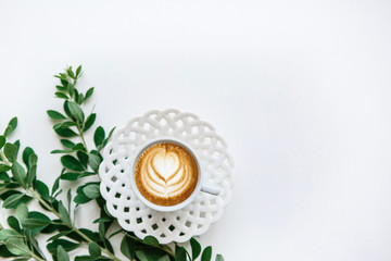 A cup of fresh fragrant cappuccino coffee next to the branches of the plant. Minimalistic design.
