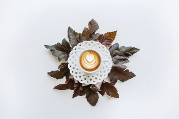 A cup of fragrant coffee cappuccino. Nearby lie autumn leaves. Simple minimalistic autumn design.