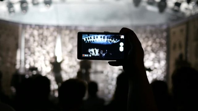 Concert phone silhouette shooting video in a fan crowd in strobe light lumiere