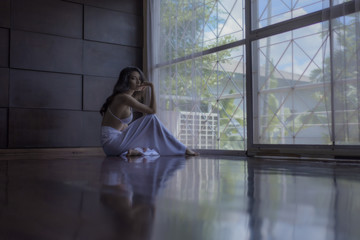 Fashion picture of a beautiful girl wearing a white dress by the window.