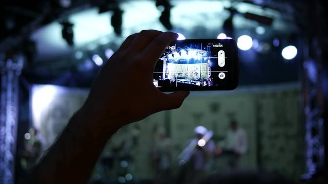 Smart phone in a hand of fan spectator shooting video of concert in lumiere flash