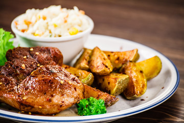 Grilled steak with baked potatoes and vegetables served on wooden table 