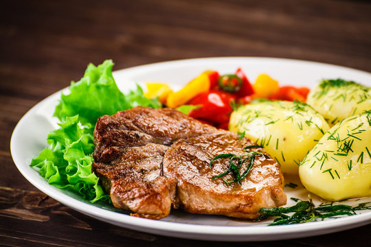 Grilled steak, baked potatoes and vegetable salad on wooden background 