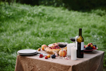 candles, wine bottle and fruits on table in garden