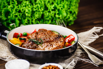 Grilled steak with vegetables in pan on wooden table