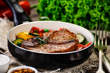 Grilled steak with vegetables in pan on wooden table