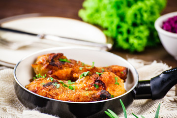 Fried drumsticks in pan with vegetables on wooden table