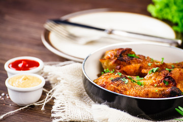 Fried drumsticks in pan with vegetables on wooden table