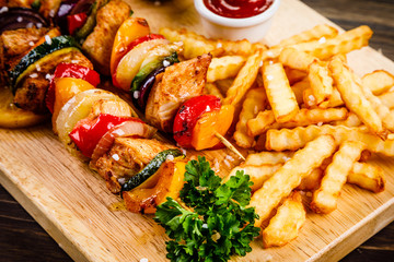 Kebabs - grilled meat with french fries and vegetables on wooden background 