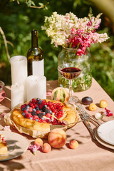 candles, wine and berries pie on table in garden