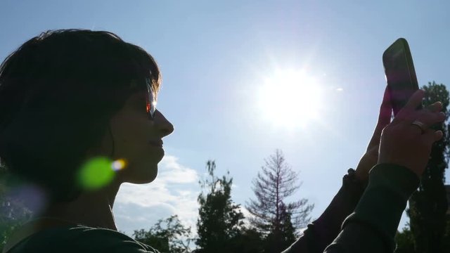 Selfie photo sliding typing smart phone - young woman sun silhouette