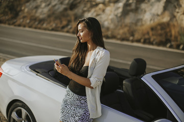 Young woman using mobile phone and standing by cabriolet car