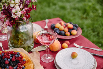 berries pie, wineglass and bouquet of flowers on table in garden