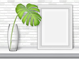 Monstera leaf and picture frame on a white table on brick wall background.