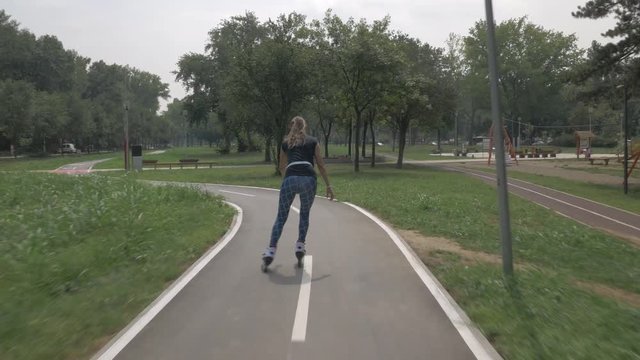 White handsom brown hair girl in tight blue pants woman riding roller skates on bike road in park, during summer day