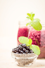 Blueberry smoothie decorated with fresh green mint leaves and raw ripe berries on yellow pastel background.