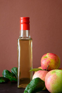 Apple vinegar in glass bottle and fresh apples on brown wooden desk