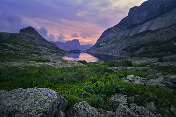 Beautiful colorful sunrise landscape of summer picturesque mountain lake with green grass and flowers