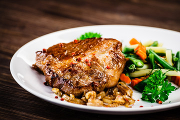 Grilled steak with vegetables on wooden background