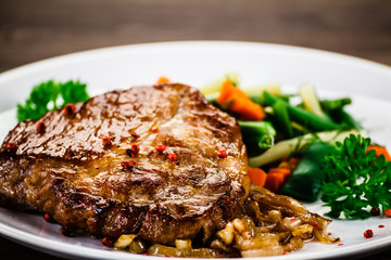 Grilled steak with vegetables on wooden background