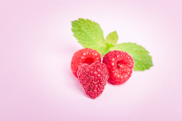 Raw ripe raspberries with fresh green mint leaf isolated on pink pastel background.