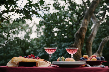 glasses of wine, berries pie and fruits on table for dinner in garden