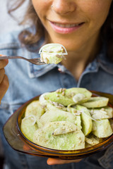 Woman tastes fresh green salad with cucumber slices or pieces with onion rings, spices and herbs as part of healthy vegan lunch or vegetarian dinner served in plate. Healthy food.
